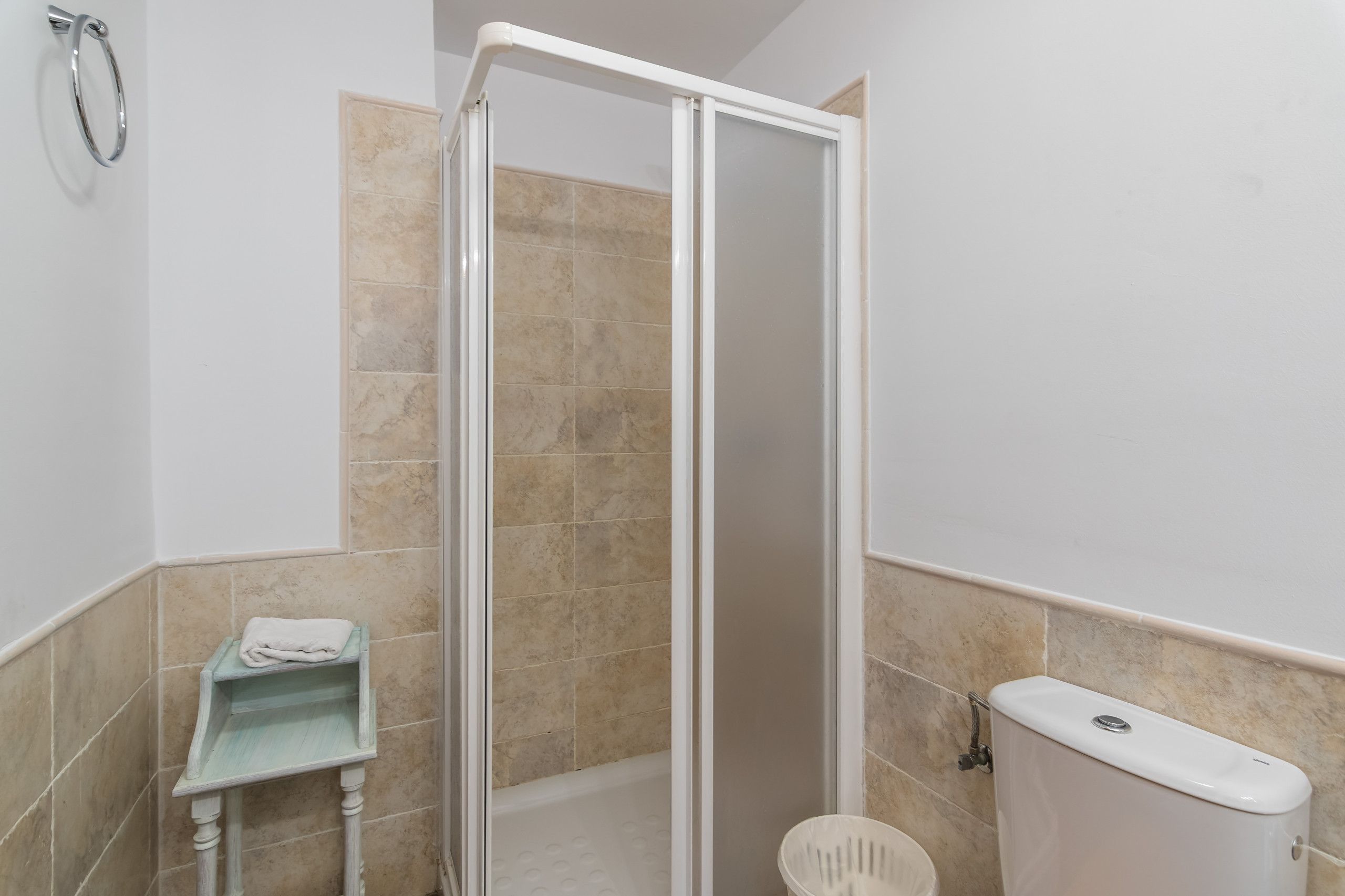 Un baño con ducha, inodoro y un pequeño estante con una toalla.