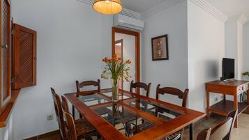 Un comedor con una mesa de madera, sillas, un jarrón con flores, una lámpara colgante y un televisor sobre un mueble de madera.