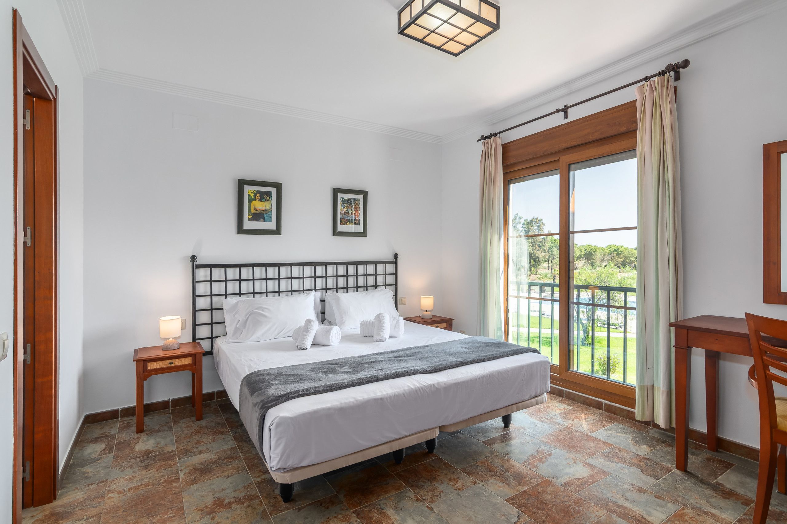 Ein Hotelzimmer mit einem Bett, zwei Nachttischlampen, einem mit Vorhängen versehenen Fenster und zwei gerahmten Bildern an der Wand.