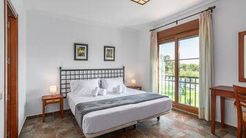 Ein Hotelzimmer mit einem Bett, zwei Nachttischlampen, einem mit Vorhängen versehenen Fenster und zwei gerahmten Bildern an der Wand.