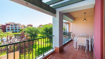 Un balcón con vistas a una zona residencial, una mesa con sillas y una lámpara colgante.
