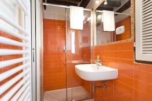 A bathroom with an orange tiled wall, a white sink, and a glass shower enclosure.
