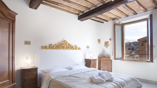 Een slaapkamer met een bed, een houten dressoir, nachtkastjes, een decoratief hoofdeinde en een raam met uitzicht op de stad.