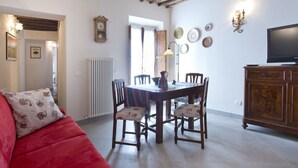 Een gezellige woonkamer met een rode bank, een houten eettafel met stoelen, een televisie en een radiator.