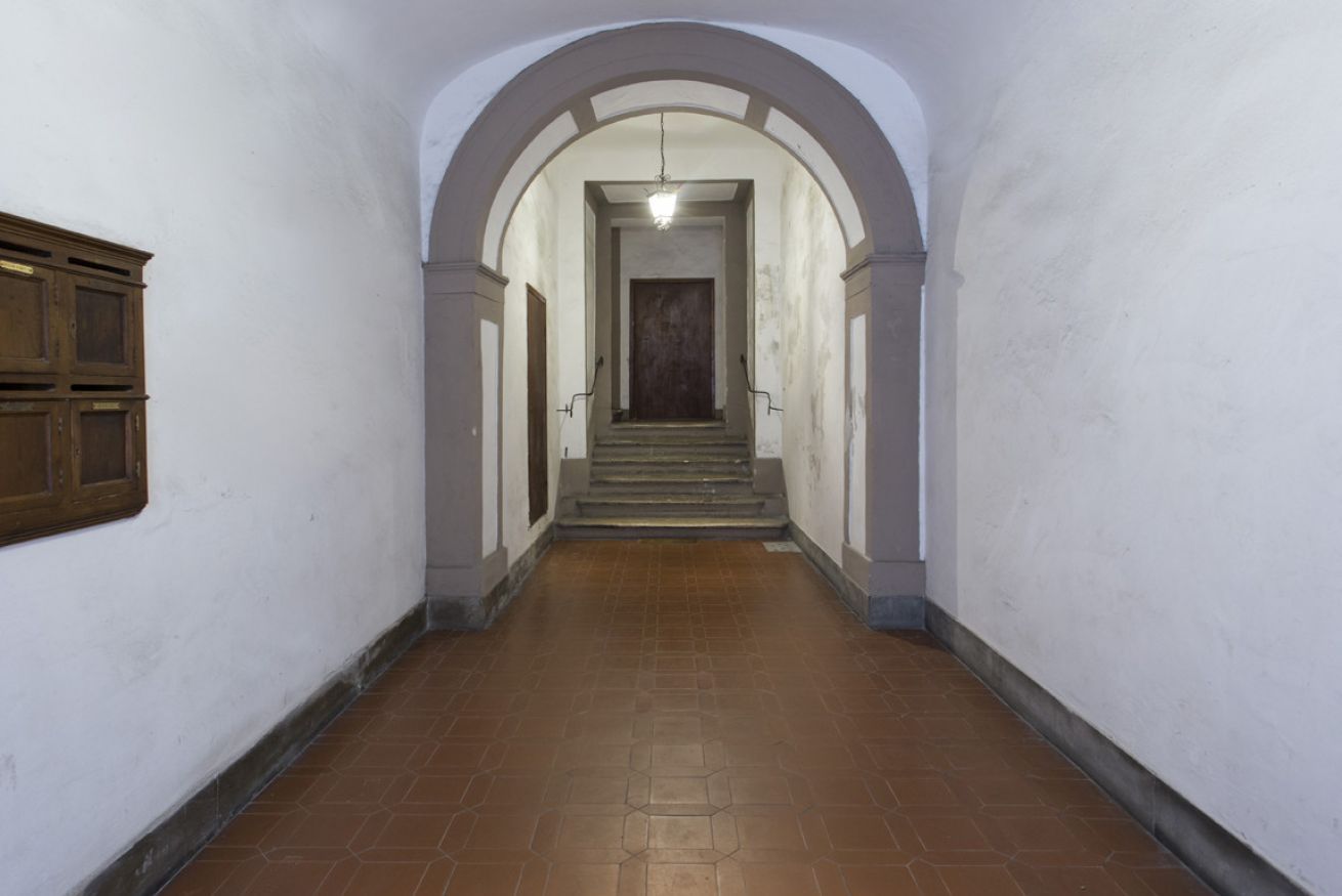 A corridor with a tiled floor, white walls, and a wooden door at the end.