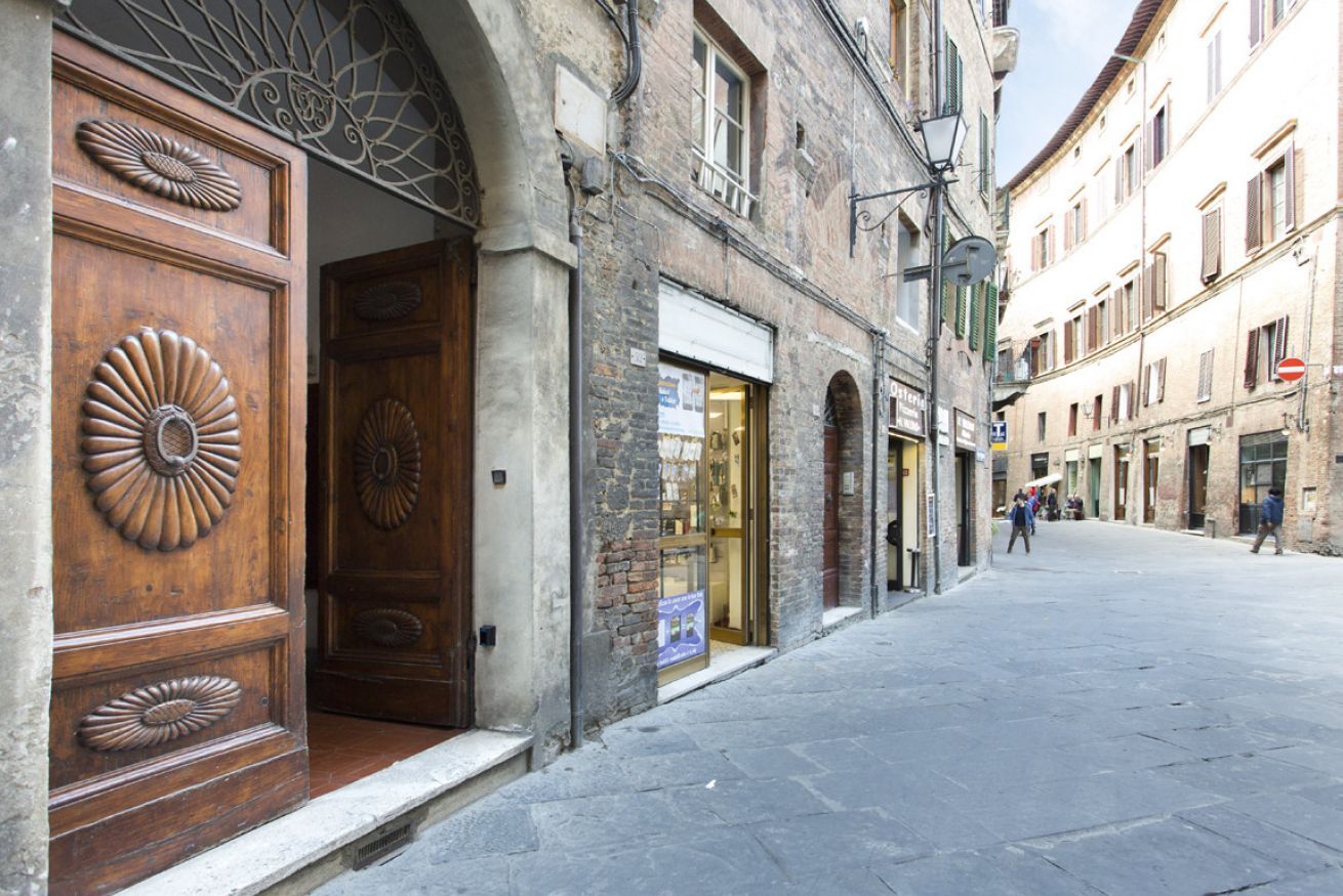 A street with a wooden door with a decorative design, a shop with a glass front, and a building with a sign.