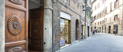 A street with a wooden door with a decorative design, a shop with a glass front, and a building with a sign.