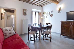 A cozy living room with a red sofa, wooden dining table, and chairs, a television, and a radiator.
