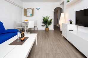 Ein modernes Wohnzimmer mit einem weißen Sofa, einem Esstisch mit Stühlen, einem Blumentopf, einem Fernseher und einer Champagnerflasche.