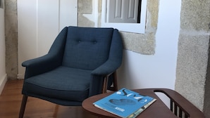A room with a blue armchair, a wooden table with a magazine, and a partially constructed wall. - The Brewmaster's House 4 | Studio Deluxe (Porto)