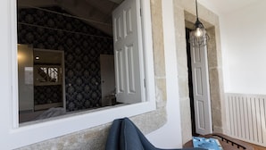 A room with a stone wall, a window with a view of a patterned wallpaper room, a door, and a hanging light fixture. - The Brewmaster's House 4 | Studio Deluxe (Porto)