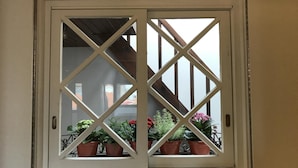 A window with a white frame and diamond-patterned glass, overlooking a balcony with potted plants. - The Brewmaster's House 4 | Studio Deluxe (Porto)