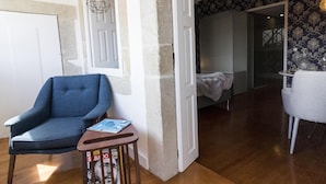 A room with a blue armchair, a small wooden table with magazines, a hanging light fixture, and a patterned wallpaper. - The Brewmaster's House 4 | Studio Deluxe (Porto)