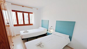 A hotel room with two single beds, a wooden wardrobe, a window with curtains, and a nightstand with a lamp. - Laura-29A - pretty holiday property with garden and private pool in Calpe (Calpe)