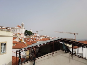 A rooftop with a metal staircase and a view of a cityscape with buildings and a construction crane. - Stylish Lisbon Apartment in Alfama (Lisbon)