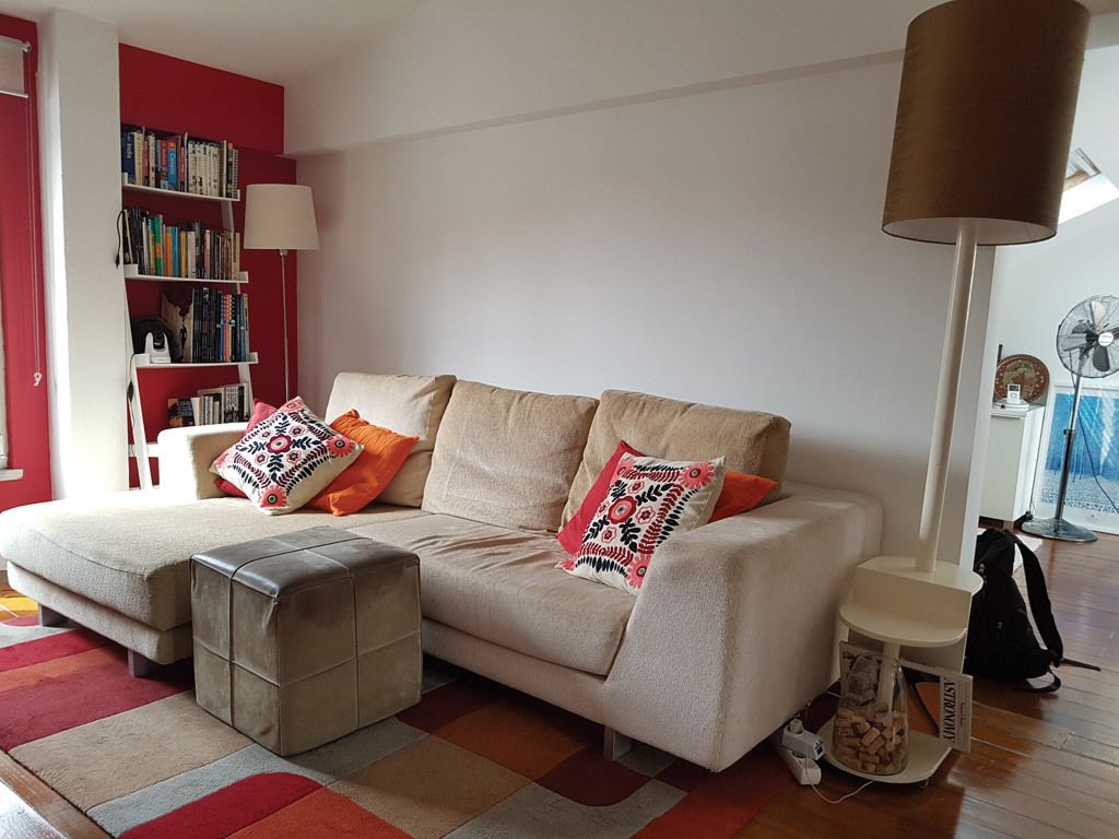Un salon avec un canapé, un pouf et une bibliothèque.