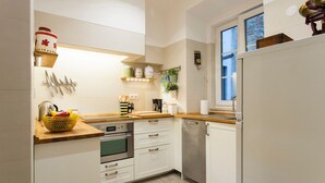 Cocina moderna con armarios blancos, encimera de madera y horno empotrado. Se observa una ventana con vistas al exterior y una planta en el alféizar.