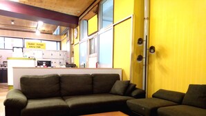 A living area with a sectional sofa, a wooden coffee table, and a kitchen in the background. - Hostel Furoya (Osaka)