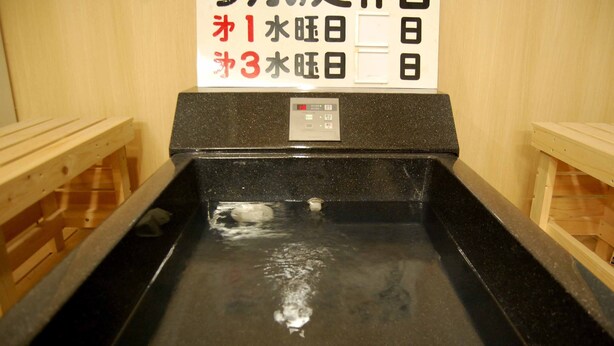A hot spring bath with wooden benches and a control panel. - Hostel Furoya (Osaka)