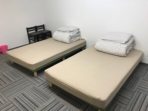 Two single beds with patterned pillows, a chair, and a pink trash bin in a room with a herringbone-patterned floor. - Hostel Furoya (Osaka)
