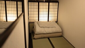 A traditional Japanese-style room with tatami flooring, a low bed with a patterned blanket, and shoji screens. - Hostel Furoya (Osaka)