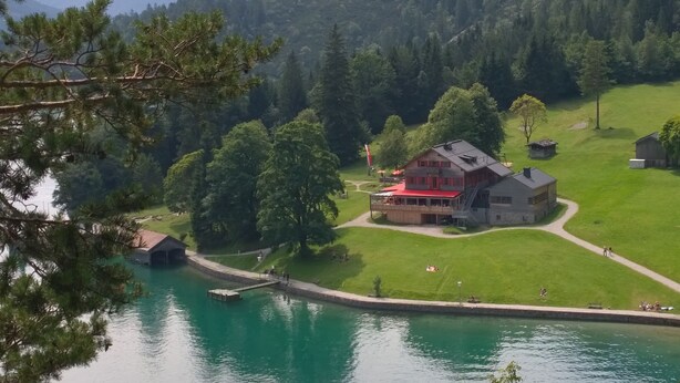 A lakeside lodge with a red-roofed main building, a dock, and a surrounding forest.