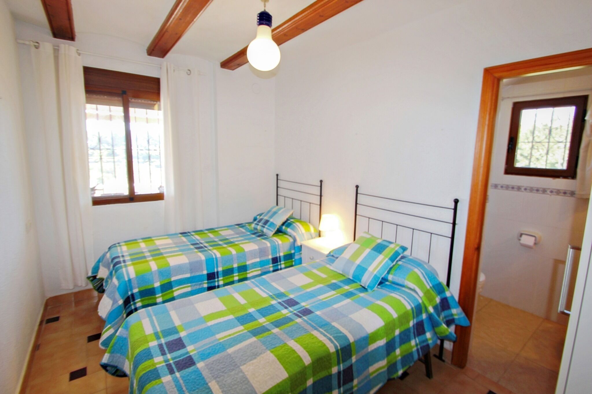 A room with two beds, a window with curtains, a ceiling fan, and a door with a window.