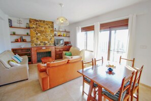 Una sala de estar con un sofá, una mesa de comedor con sillas, un televisor y una pared de piedra.