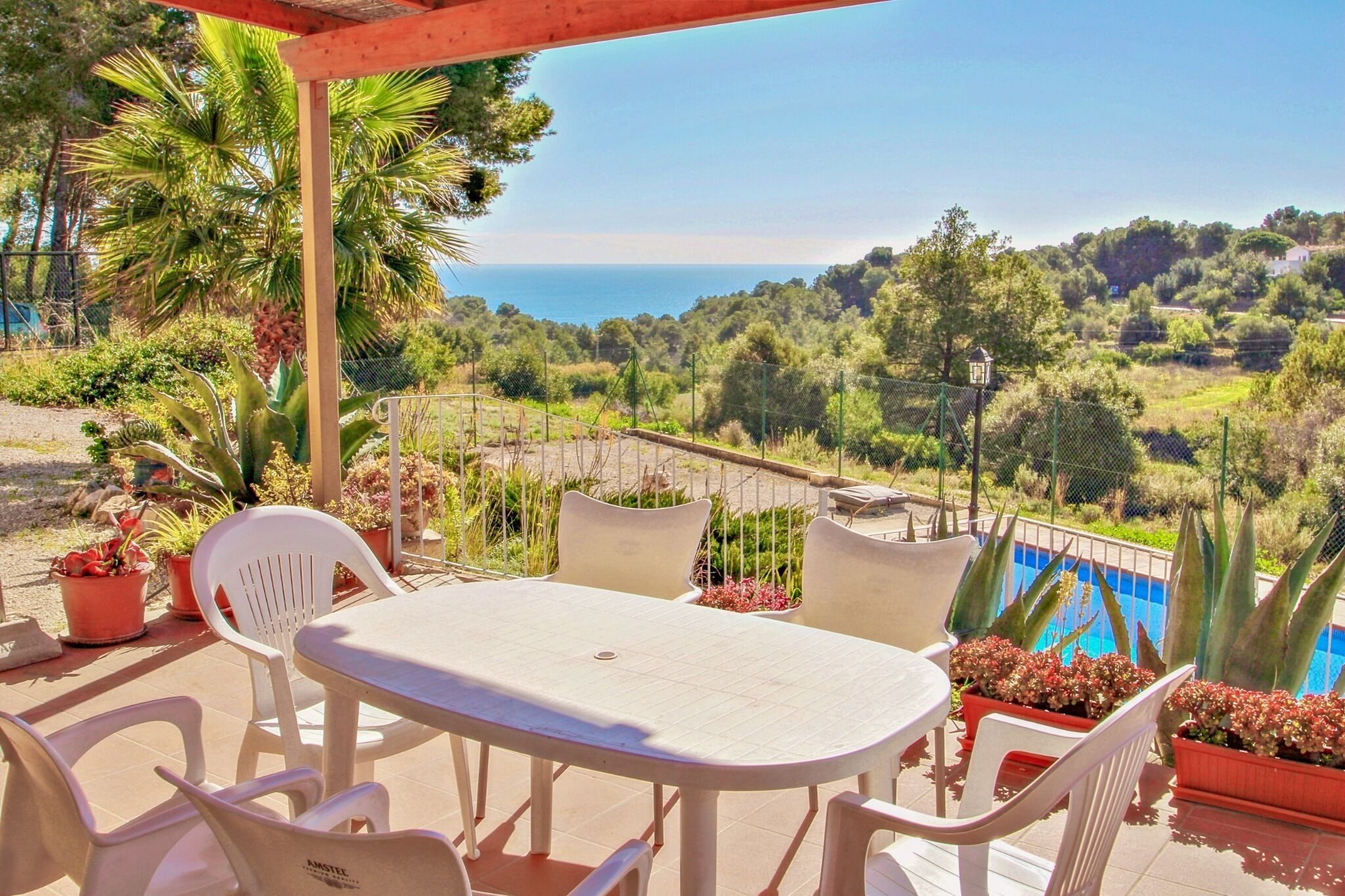 Une terrasse avec une table et des chaises, donnant sur une piscine et offrant une vue panoramique sur la mer et les collines.