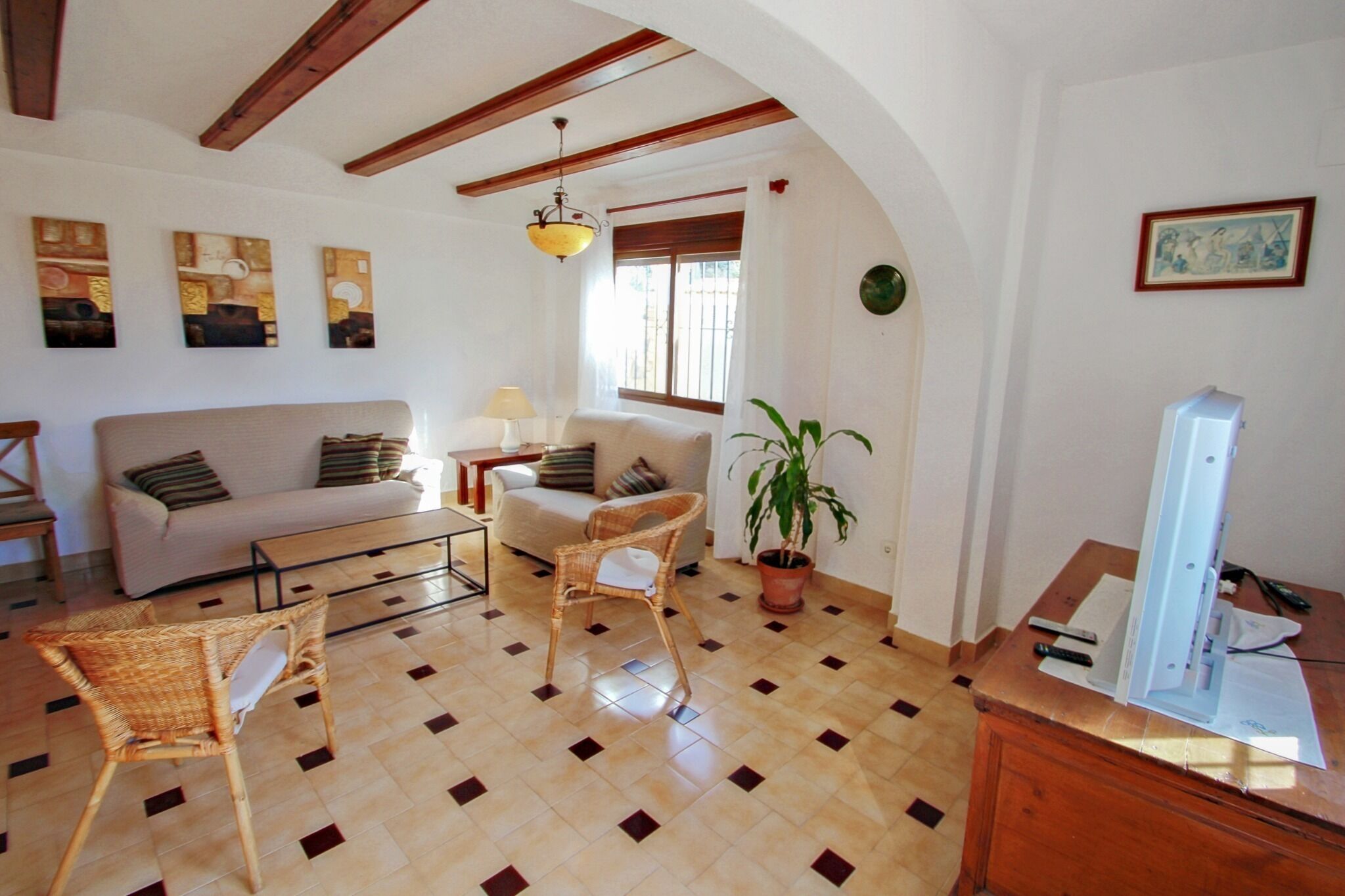 A living room with a sofa, two chairs, a coffee table, a TV, a lamp, and a potted plant.