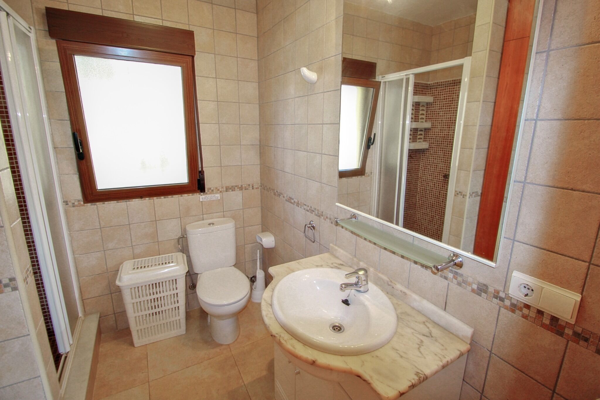A bathroom with a toilet, a sink, a mirror, and a window.