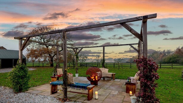 Une terrasse extérieure dotée d’une pergola en bois, de sièges et d’un foyer.