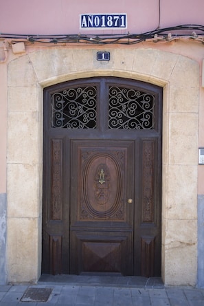 Uma porta de madeira com esculturas detalhadas e um bate-prato de latão, embutida em um edifício de pedra com uma placa acima que diz "ANO1871".
