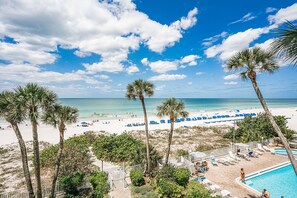 A beach view with palm trees, a pool, and beach chairs.