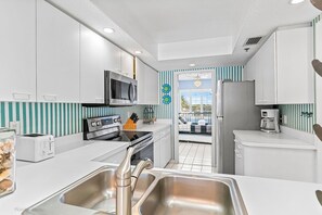 A modern kitchen with white cabinets, stainless steel appliances, and a view to a balcony.