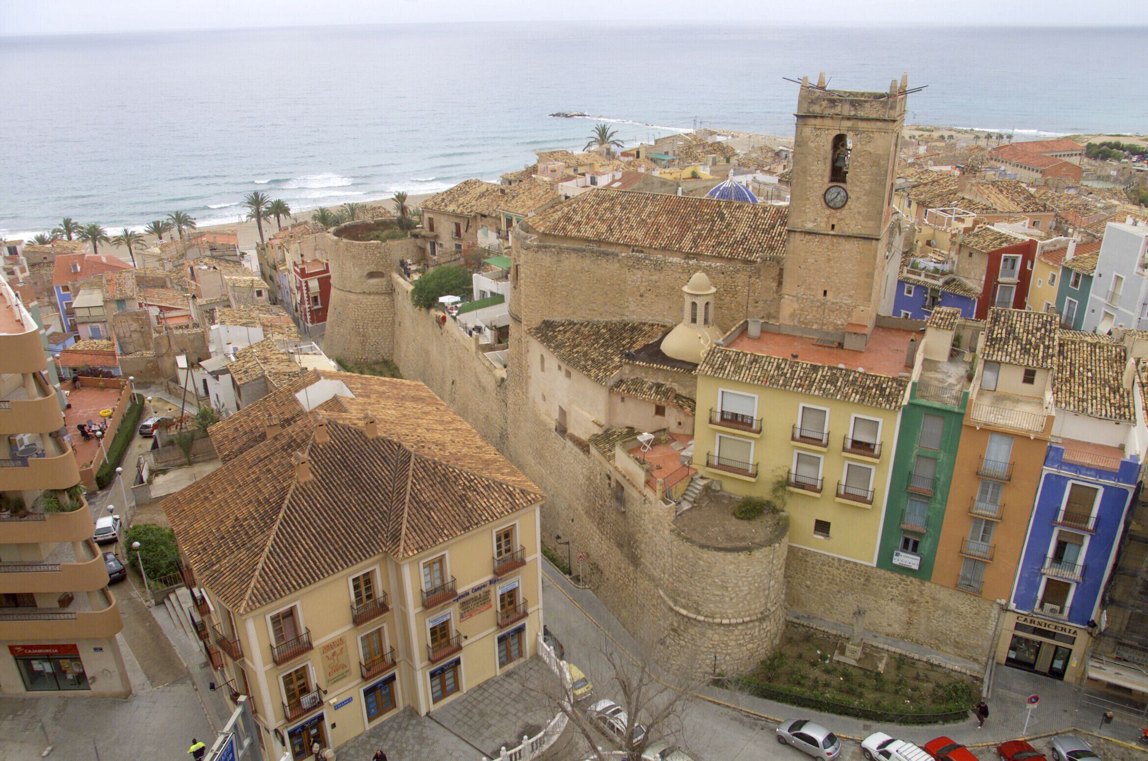 A coastal town with historic buildings, a prominent tower, and a view of the sea.
