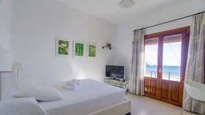 A bedroom with a bed, a TV, a balcony with curtains, and framed pictures on the wall. - MAR  - ESTUDIO CON VISTAS AL MAR (Villajoyosa)