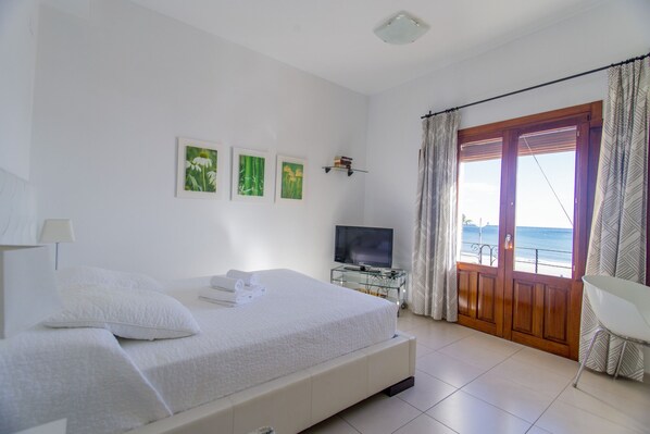 Un dormitorio con cama, televisor, balcón con cortinas y cuadros en la pared.