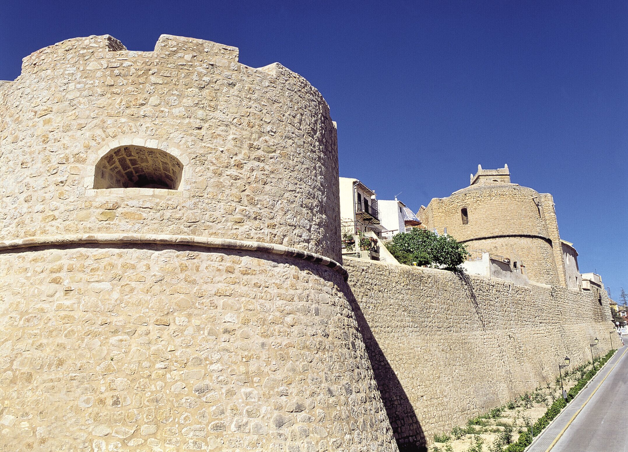 Une forteresse en pierre dotée d’une tour ronde et d’un bâtiment rectangulaire avec un balcon.