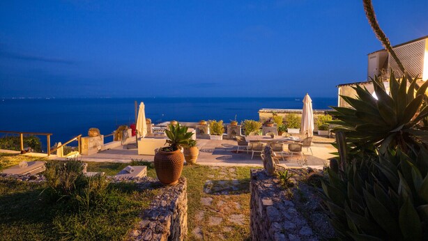 Une terrasse avec des sièges extérieurs, des plantes en pot et une vue sur la mer.