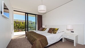 Et moderne hotelværelse med en stor seng, et natbord med lampe og udsigt til grønne områder.