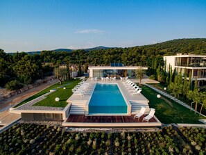 Un complex turístic modern amb una piscina gran, gandules i vistes als turons circumdants.