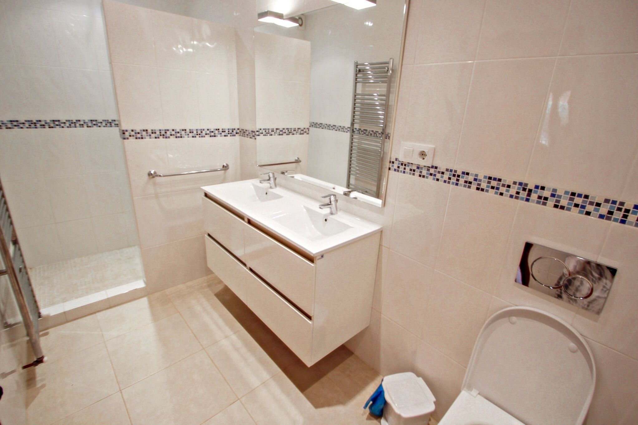 Et moderne badeværelse med brusekabine, dobbelt vask og toilet.