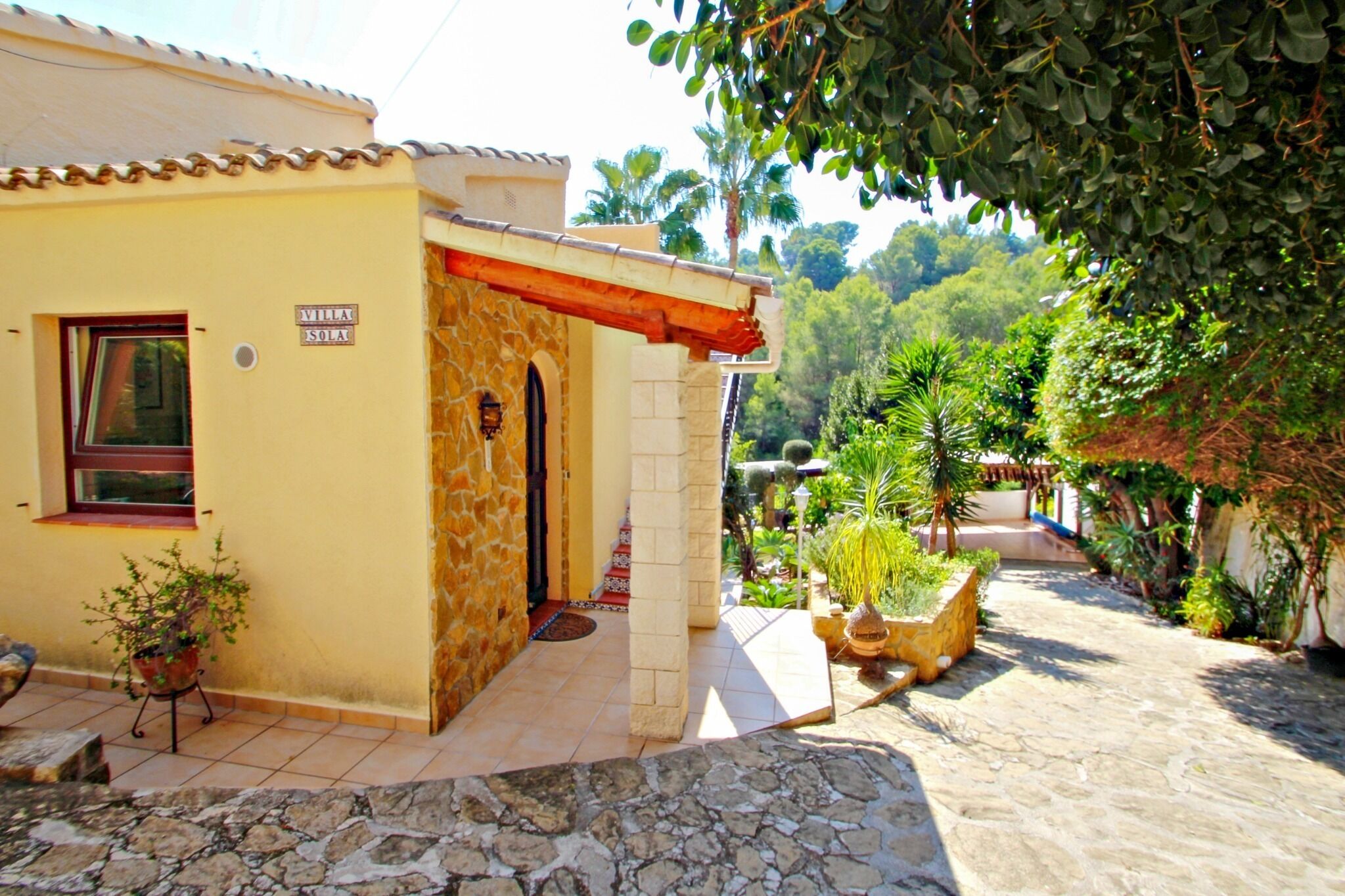 Una villa con fachada de piedra, un patio empedrado y un jardín con diversas plantas.