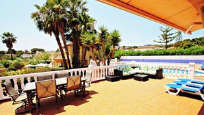 Una terraza con mobiliario exterior, piscina y palmeras.
