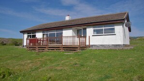 A single-story house with a fenced porch, white exterior walls, and a brown roof. - Steading Holidays - Ceol na Mara (Acharacle)
