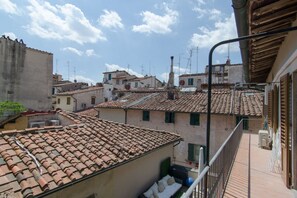 A rooftop terrace with terracotta tiles, a balcony with a metal railing, and a view of adjacent buildings with similar architecture.