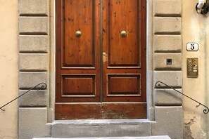 A double wooden door with brass handles, flanked by stone walls, and a number plaque indicating the location.