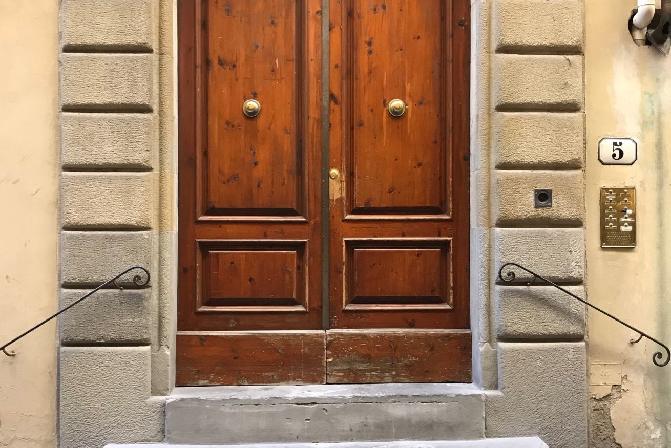 A double wooden door with brass handles, flanked by brick walls, and a small step leading up to it.