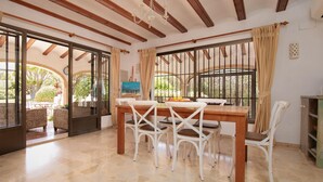 A dining area with a wooden table and white chairs, large windows with curtains, and a view of the outdoors. - El Tesorito Javea - Javea, Costa Blanca (Javea)